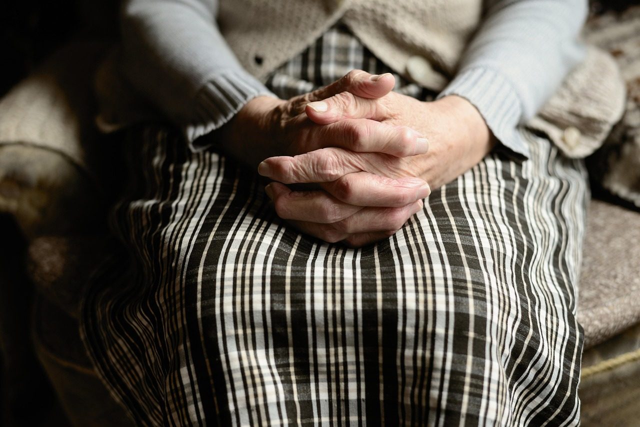 An older adult’s hands folded in their lap